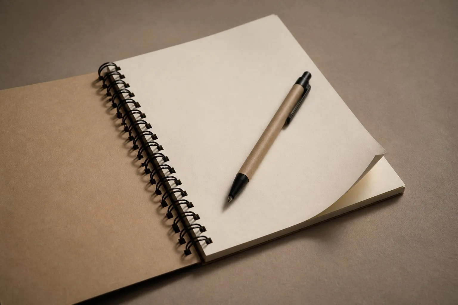 An open spiral-bound notebook on a blank page, with a pen resting across it.